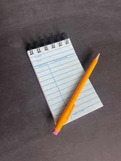 a notepad with a yellow pencil next to it on top of a black surface