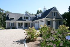 a large gray house with lots of windows and shutters on the front, surrounded by flowers