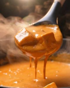 a ladle full of soup being stirred by a wooden spoon with some food in it