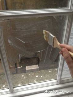 a hand holding a paintbrush in front of a window with plastic covering the windows