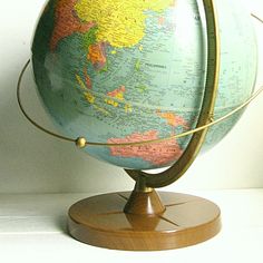 an old world globe is sitting on a wooden stand in front of a white wall