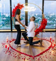 a man kneeling down next to a woman in front of a heart with roses on it