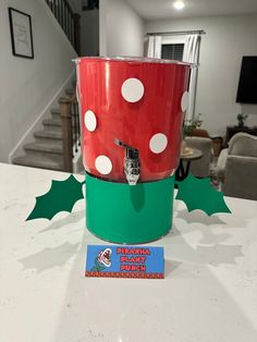 a red and green cup sitting on top of a table next to a christmas card