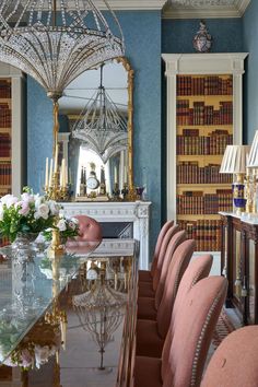 an elegant dining room with blue walls and chandelier above the table, along with pink upholstered chairs