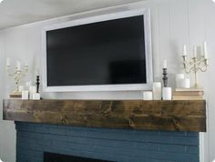 a flat screen tv mounted above a fireplace with candles on the mantel below it