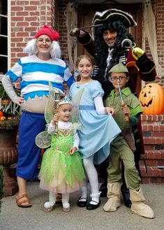 a group of people standing next to each other wearing costumes and holding pumpkins in front of a brick building