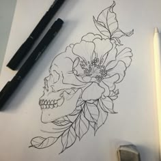 a drawing of a skull with flowers and leaves on paper next to two markers,