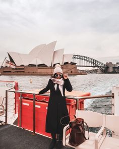 a woman standing on the deck of a boat in front of the sydney opera house