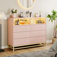 a pink dresser in a white room with a mirror on the wall and various items on it