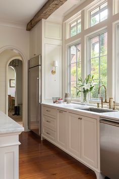 a kitchen with wooden floors and white cabinets, an island countertop and two windows