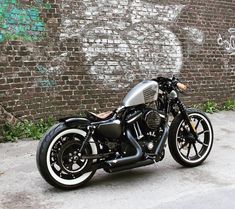 a black and silver motorcycle parked in front of a brick wall with graffiti on it