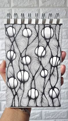 a hand holding up a notebook with black and white designs on it