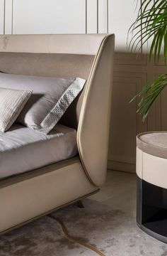 a bed with white sheets and pillows in a room next to a potted plant