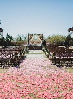 an outdoor wedding ceremony with pink petals on the ground and chairs in the aisle to the side