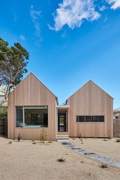 two wooden houses sitting next to each other on top of a dirt field with trees in the background