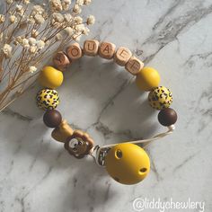 a yellow and brown beaded bracelet with the word baby spelled on it next to some dried flowers