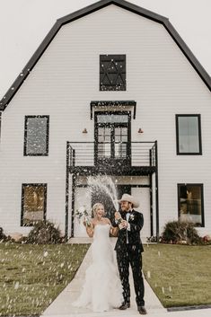 a bride and groom standing in front of a large white house with snow falling on them