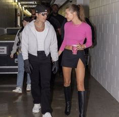 a man and woman are walking down the hallway with one holding a drink in her hand