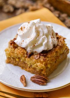 a piece of cake on a plate with whipped cream and pecans in the background