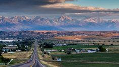 an empty highway with mountains in the background and clouds in the sky above it,