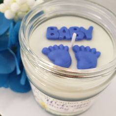 two baby hand and foot candles in a jar with blue flowers behind it on a table