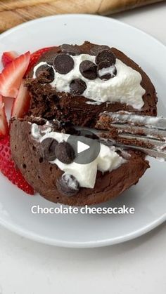 chocolate cheesecake with whipped cream and strawberries on white plate next to pastry knife