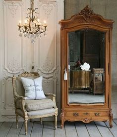 a chair and mirror sitting in front of a wall with chandelier hanging from it