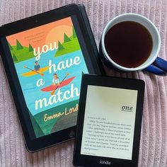 an electronic book next to a cup of tea and a tablet on a pink blanket