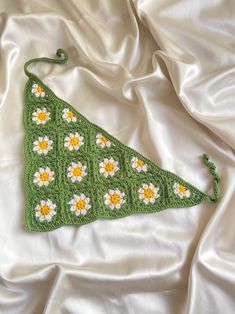 a green crocheted triangle with white and yellow flowers