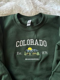 Colorado, stand up! Comfy sweatshirt with Colorado in a varsity-like font featuring a mountain design. This pullover Crewneck will keep you stylish and warm with its fleece lined fit.  You can add names on the sleeve for $5 extra!  This sweatshirt is available in 6 colors:  ✨ Military Green ✨ Forest Green ✨ Sand ✨ White (words will be in black) ✨ Light Blue ✨ Navy ✨ Heather Gray If there is a color you have in mind other than the ones available, send me a message and I can help! -Sweatshirt bran Colorado Nature, Colorado Sweatshirt, Navy Crewneck, Green Crewneck, Colorado Mountain, Mountain Designs, Embroidered Crewneck, Fun Sweatshirts, For Her Gifts