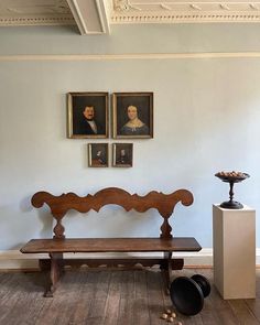 a wooden bench sitting in front of two pictures on the wall next to a vase