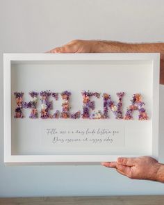 a person holding up a framed sign with flowers in the letters spelling it's birth