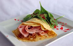 a white plate topped with ham and tortilla wrap on top of lettuce