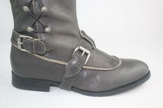 Grey boots make an excellent accompaniment to almost any outfit. Metal studs run vertically up the side with leather laces. Together the leather strap around the arch gives and tan trim around the base of your toes gives these boots an equestrian feel with a unique tailored twist. Approx: 1/4" heel Shiny studs add edgy style to these tall leather boots from J. Litvack. Featuring a round toe, dual adjustable ankle straps with side buckle closure, and leather weaving throughout the side studs. Leather Lace-up Boots With Rivets, Leather Knee-high Moto Boots With Rivets, Leather Moto Boots With Grommets For Fall, Leather Lace-up Moto Boots With Rivets, Western Leather Boots With Rivets, Leather Boots With Rivets And Snip Toe, Western Leather Boots With Silver Studs, Leather Moto Boots With Silver Studs For Fall, Leather Ankle Moto Boots With Lacing