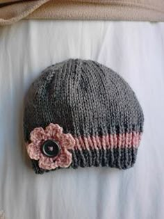 a knitted hat with a flower on it laying on top of a white sheet