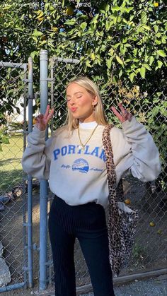 a woman standing in front of a chain link fence wearing a sweater with the word portland on it