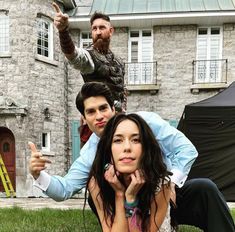 two people are posing for a photo in front of a house with a man on his shoulders