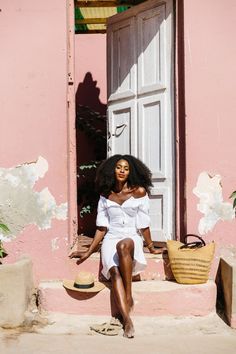 a woman sitting on steps in front of a pink building with white door and window