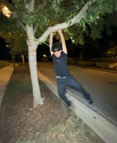 a man in black shirt standing next to a tree and holding his arms up with both hands