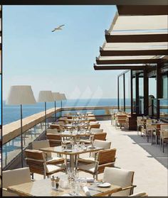 an outdoor dining area overlooking the ocean with seagulls flying over it and empty tables