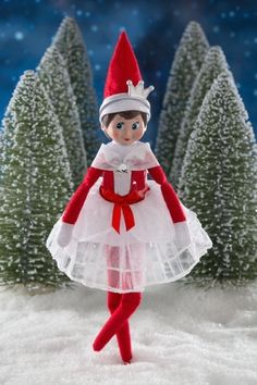 an elf is standing in the snow wearing a white and red tutu skirt, with trees behind her