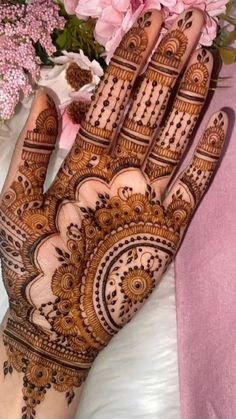 a henna on someone's hand with flowers in the back ground and pink flowers behind it