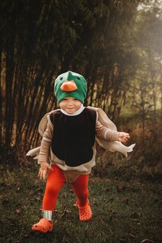 a toddler in an orange and black outfit is walking through the grass with trees behind him