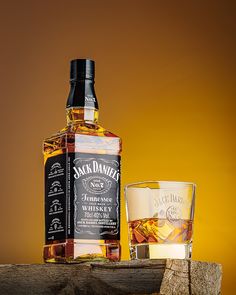 a bottle of jack daniels whiskey next to a shot glass on a wooden table with an orange background