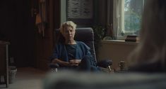 an older woman sitting in a chair looking out the window