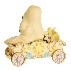 a ceramic figurine of a woman riding in a toy car with flowers on the side