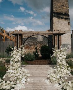 an outdoor wedding ceremony with white flowers on the arch and brick building in the background