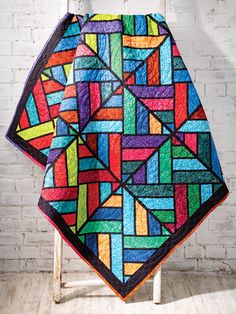 a multicolored quilt hanging on a white chair in front of a brick wall