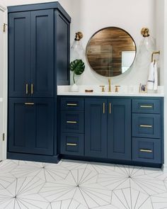 a bathroom with blue cabinetry and white tile flooring, gold accents on the mirror