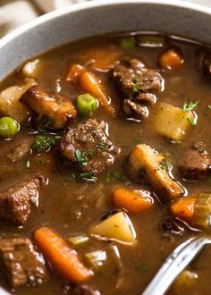 a bowl of beef stew with carrots, potatoes and peas